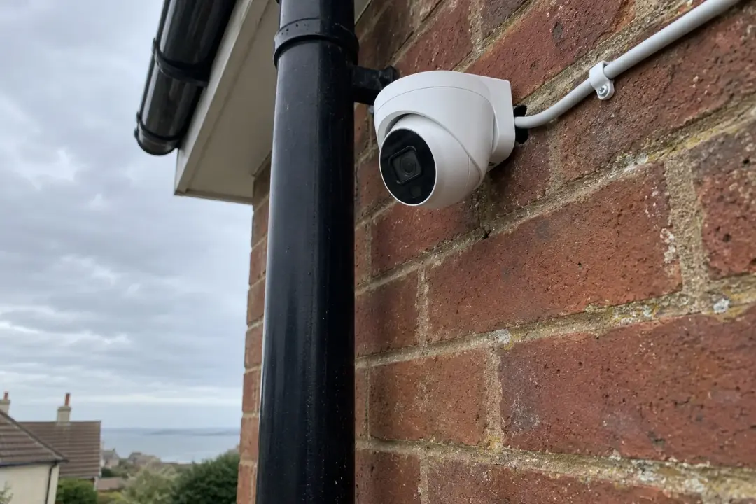 A white turret camera on a red brick wall with its cable clipped up the brickwork