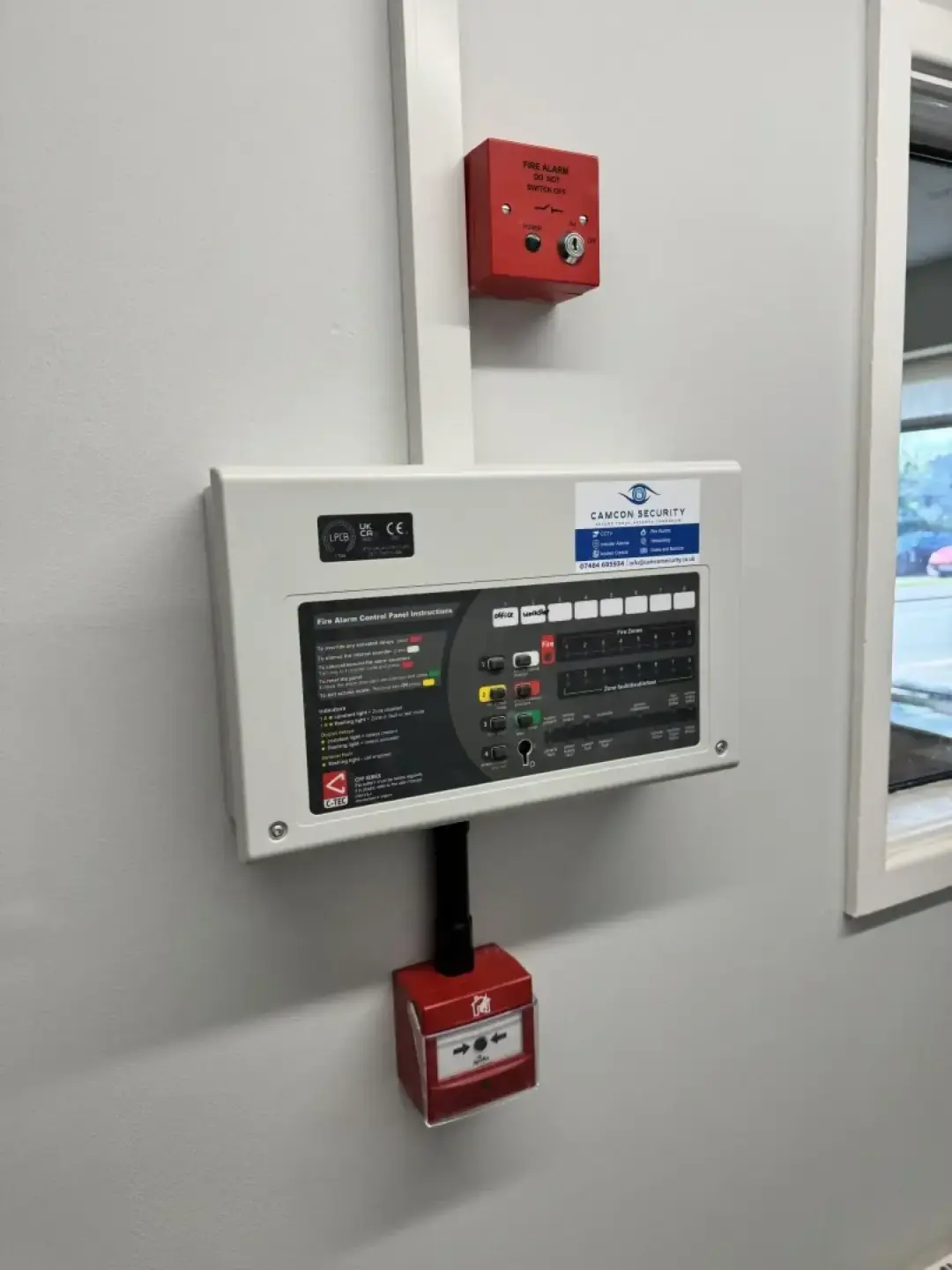 A fire alarm control panel with a manual call point above and below it