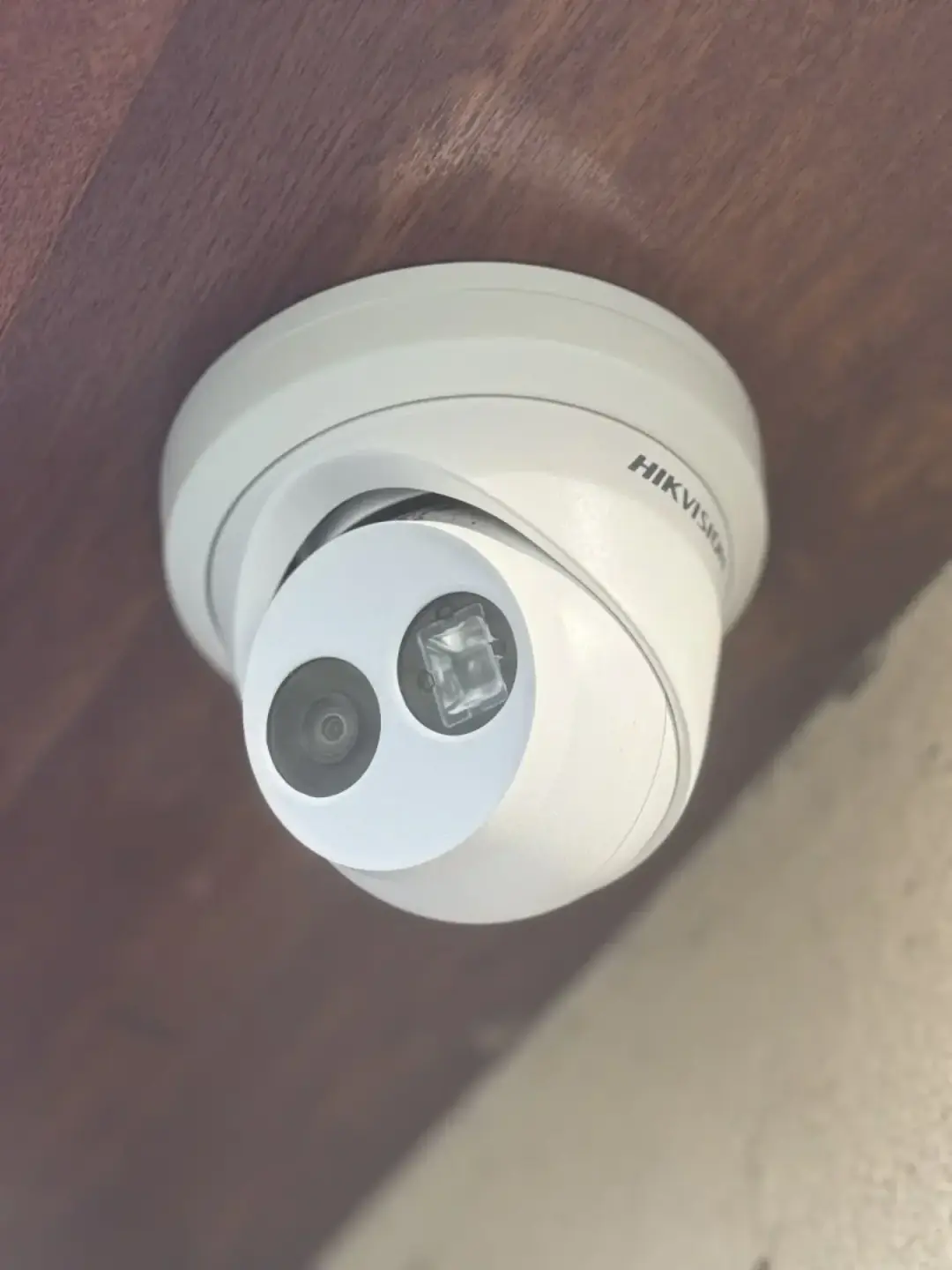 A white Hikvision turret camera fitted under a dark timber soffit
